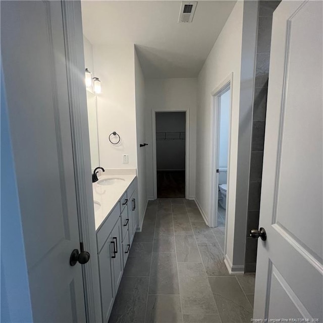 full bath with a walk in closet, toilet, a sink, visible vents, and double vanity