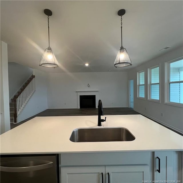 kitchen with light countertops, dishwasher, a fireplace, a sink, and open floor plan