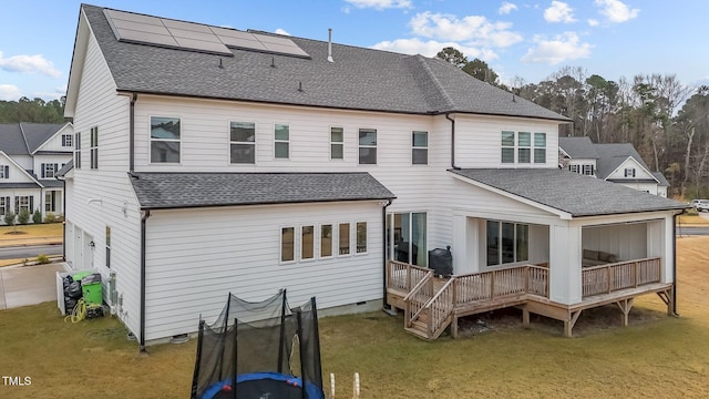 rear view of property with solar panels, a lawn, a deck, and a trampoline