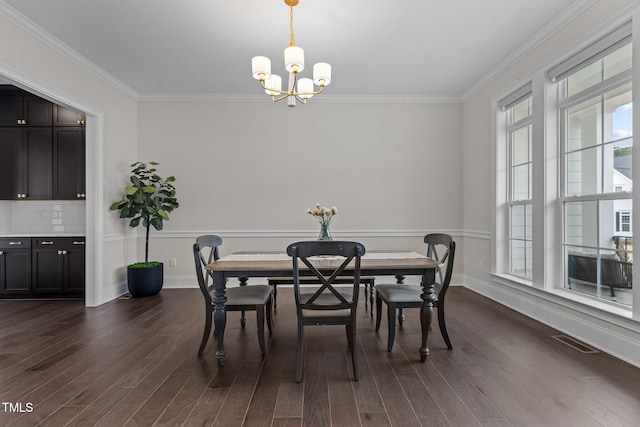 dining area with crown molding, dark wood-type flooring, and an inviting chandelier