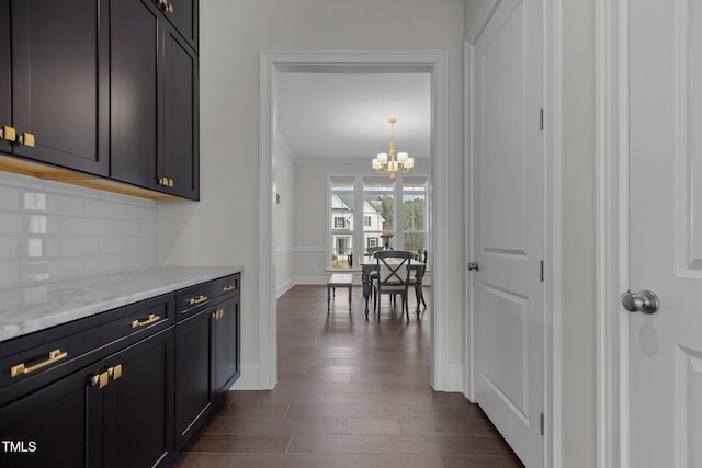 kitchen with dark wood-type flooring, light stone counters, a notable chandelier, pendant lighting, and decorative backsplash