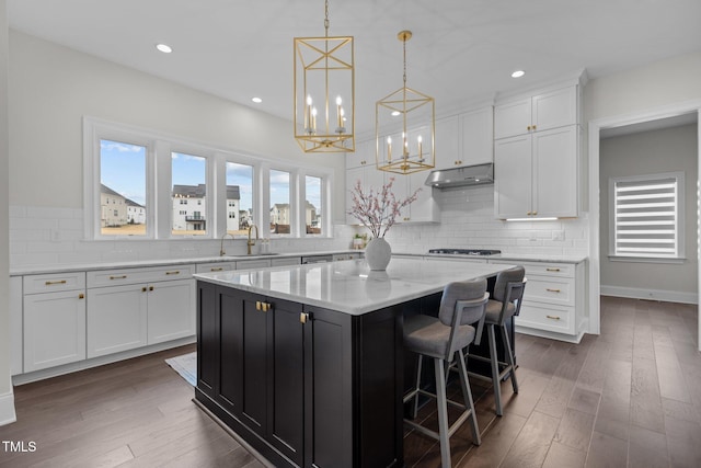 kitchen with a center island, dark wood-type flooring, white cabinets, sink, and a kitchen bar