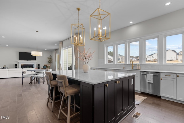 kitchen with hardwood / wood-style floors, dishwasher, a center island, hanging light fixtures, and light stone counters