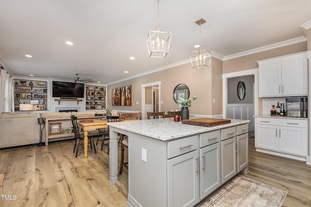 kitchen with a breakfast bar area, light stone counters, a center island, pendant lighting, and ceiling fan