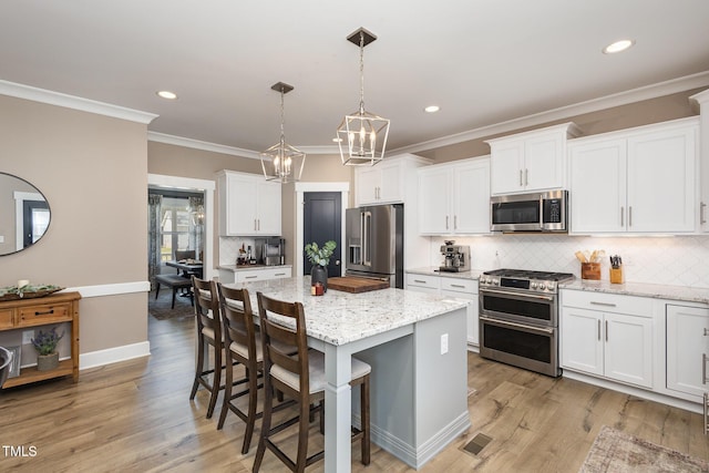 kitchen featuring a kitchen island, white cabinetry, hanging light fixtures, light stone counters, and stainless steel appliances