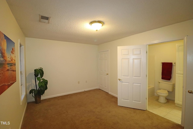 unfurnished bedroom featuring light tile patterned floors, a textured ceiling, and connected bathroom