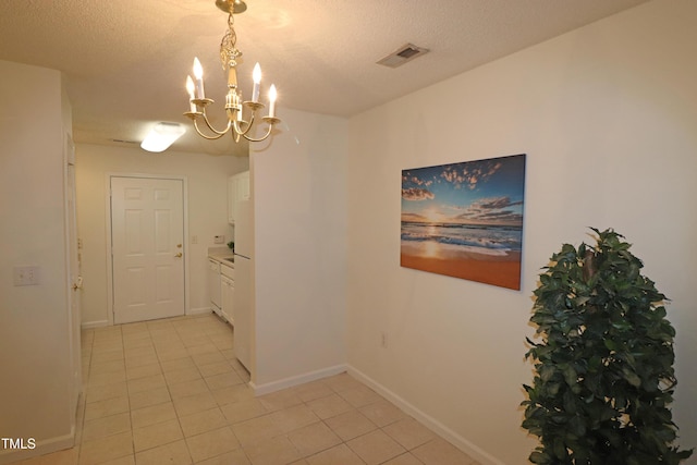 corridor featuring light tile patterned floors, a textured ceiling, and an inviting chandelier