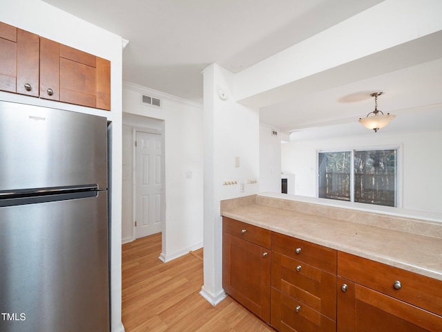 kitchen featuring ornamental molding, light wood-type flooring, stainless steel refrigerator, and decorative light fixtures