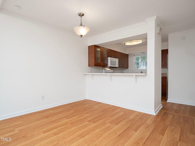 kitchen with crown molding, light hardwood / wood-style flooring, kitchen peninsula, and a kitchen bar