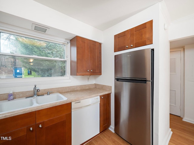 kitchen featuring sink, crown molding, stainless steel fridge, white dishwasher, and light hardwood / wood-style floors