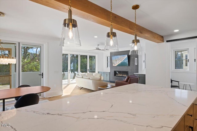 kitchen with a tile fireplace, light stone counters, beam ceiling, and decorative light fixtures