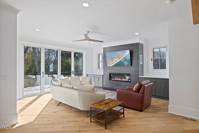 living room with a tiled fireplace, ornamental molding, ceiling fan, and light hardwood / wood-style floors