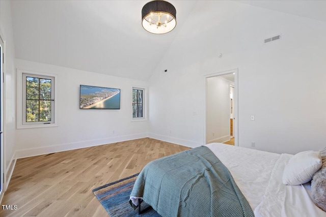 bedroom with high vaulted ceiling, a chandelier, and light wood-type flooring