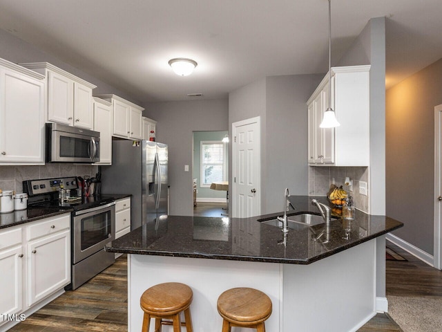 kitchen featuring appliances with stainless steel finishes, backsplash, dark stone counters, dark wood-type flooring, and hanging light fixtures