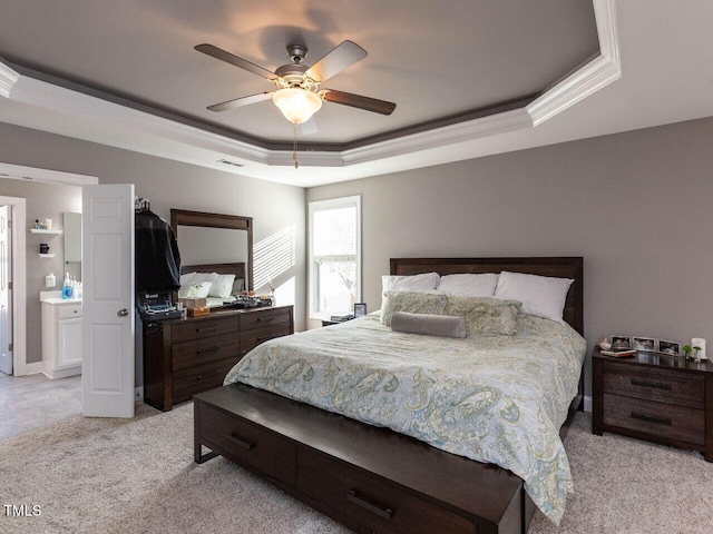 carpeted bedroom featuring a tray ceiling, ensuite bath, ceiling fan, and ornamental molding