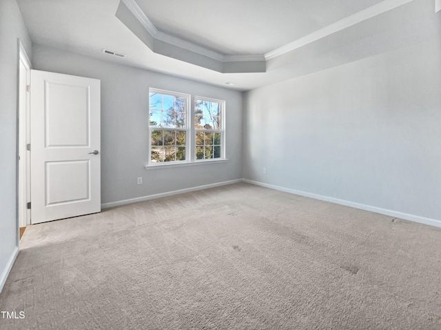 empty room with a raised ceiling, light colored carpet, and crown molding