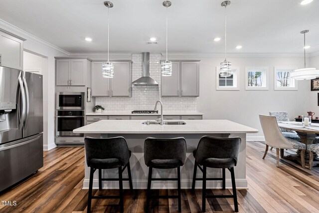 kitchen with hardwood / wood-style floors, decorative light fixtures, wall chimney range hood, and appliances with stainless steel finishes