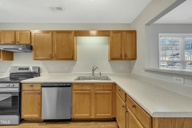 kitchen with appliances with stainless steel finishes, light wood-type flooring, a textured ceiling, and sink