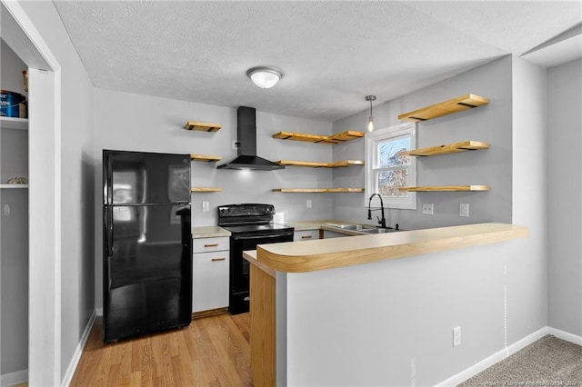 kitchen with light wood-type flooring, wall chimney exhaust hood, a textured ceiling, sink, and black appliances