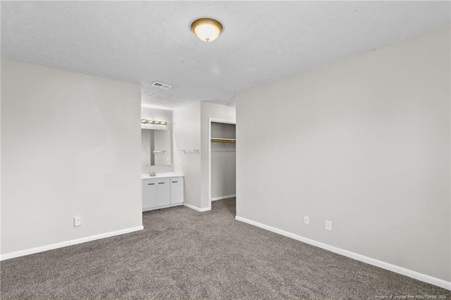 unfurnished bedroom featuring carpet flooring, ensuite bath, a closet, and a textured ceiling