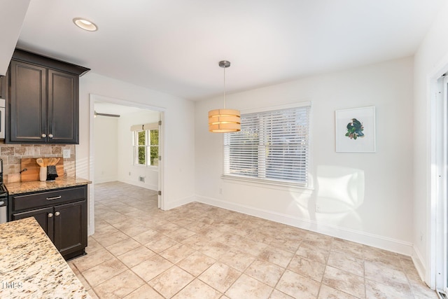 kitchen with decorative backsplash, dark brown cabinets, light stone counters, and hanging light fixtures