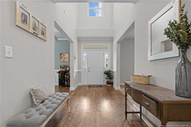 entryway with wood-type flooring, a towering ceiling, a wealth of natural light, and ornamental molding