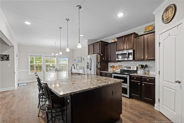 kitchen featuring ornamental molding, an island with sink, appliances with stainless steel finishes, decorative light fixtures, and a kitchen bar