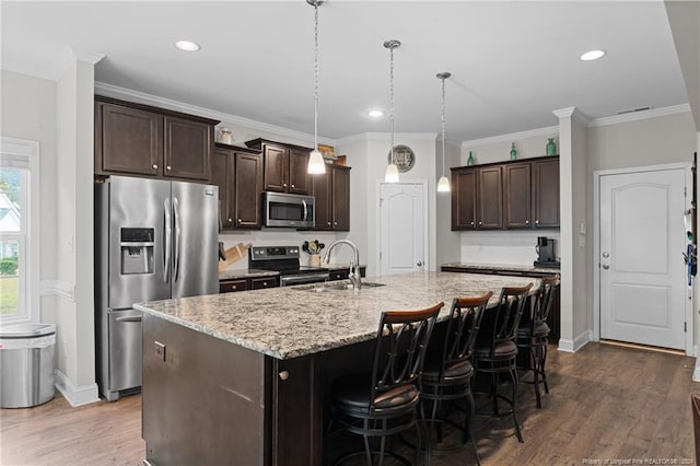 kitchen with sink, dark wood-type flooring, stainless steel appliances, decorative light fixtures, and a kitchen island with sink