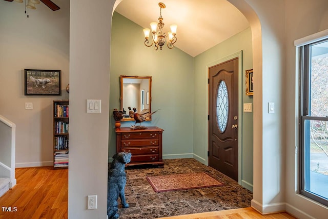 foyer with ceiling fan with notable chandelier, plenty of natural light, vaulted ceiling, and light wood-type flooring