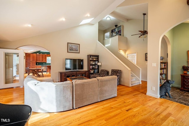 living room with beam ceiling, high vaulted ceiling, ceiling fan, and light wood-type flooring