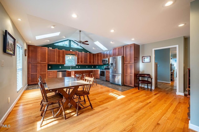 dining room with sink, ceiling fan, vaulted ceiling with skylight, and light wood-type flooring