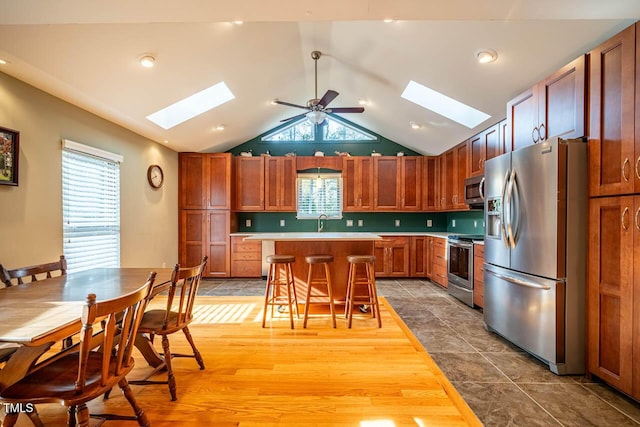 kitchen featuring lofted ceiling with skylight, ceiling fan, appliances with stainless steel finishes, a kitchen island, and a breakfast bar area