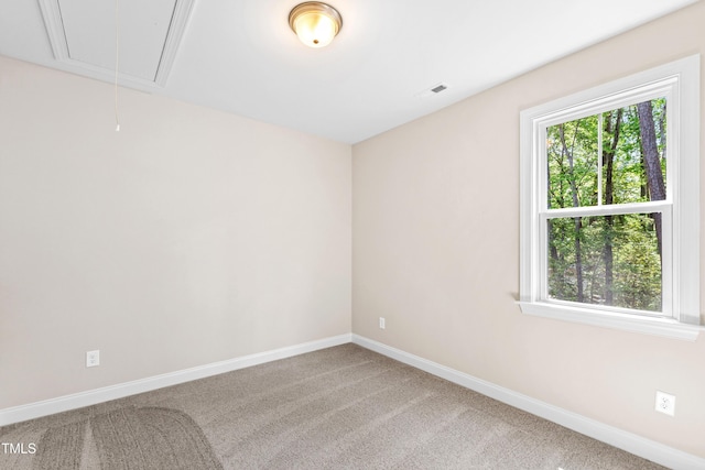 carpeted spare room with baseboards, attic access, and visible vents
