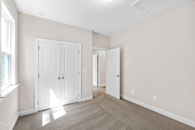 unfurnished bedroom featuring baseboards, attic access, carpet, and a closet