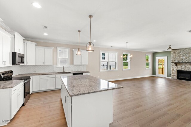 kitchen with backsplash, appliances with stainless steel finishes, a center island, a sink, and ceiling fan with notable chandelier