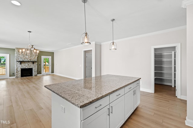 kitchen with baseboards, a center island, white cabinets, light stone counters, and light wood finished floors