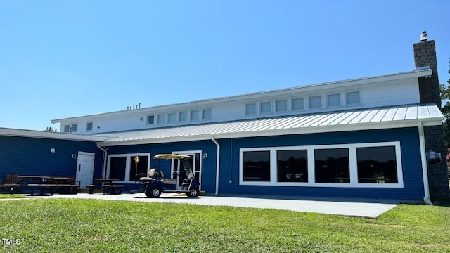 rear view of property featuring a standing seam roof, a chimney, a patio area, a lawn, and metal roof