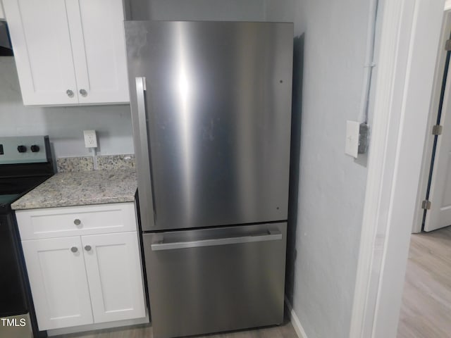 kitchen with stainless steel fridge, light stone counters, white cabinets, light hardwood / wood-style floors, and black / electric stove