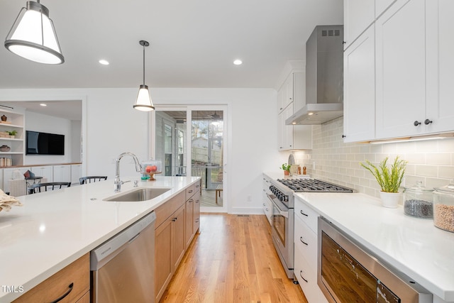 kitchen featuring pendant lighting, wall chimney range hood, sink, appliances with stainless steel finishes, and white cabinetry