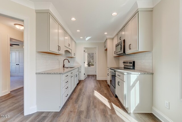 kitchen featuring white cabinets, sink, light stone countertops, light wood-type flooring, and stainless steel appliances