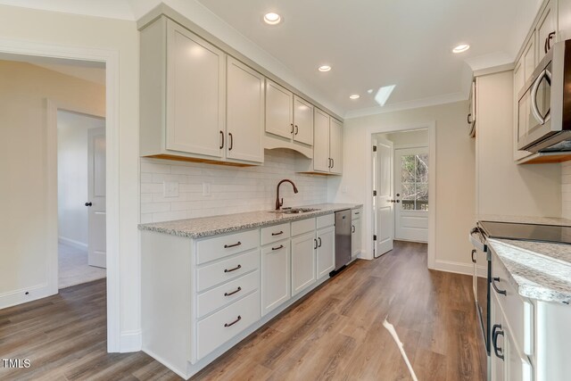 kitchen with sink, stainless steel appliances, light stone counters, light hardwood / wood-style flooring, and crown molding