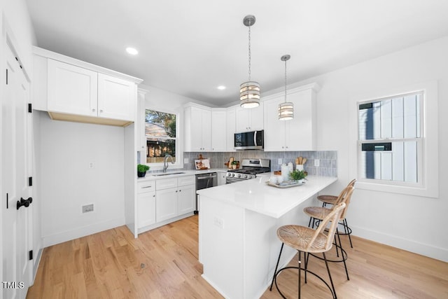 kitchen featuring white cabinetry, hanging light fixtures, light hardwood / wood-style flooring, kitchen peninsula, and appliances with stainless steel finishes