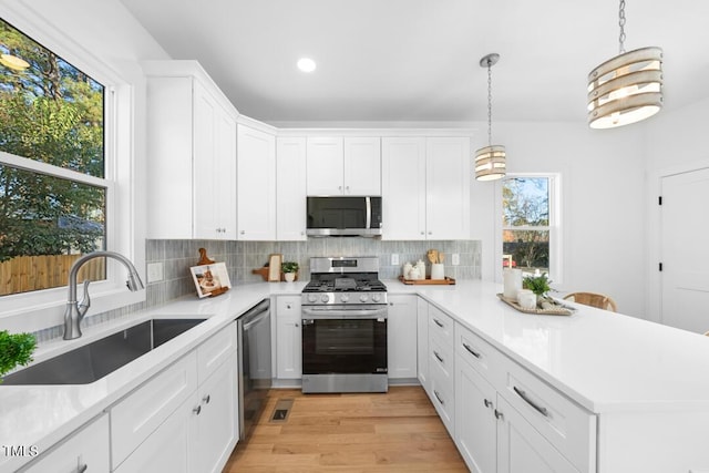 kitchen featuring white cabinets, hanging light fixtures, sink, appliances with stainless steel finishes, and light hardwood / wood-style floors