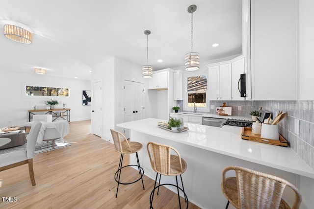 kitchen with white cabinetry, sink, light hardwood / wood-style flooring, pendant lighting, and decorative backsplash