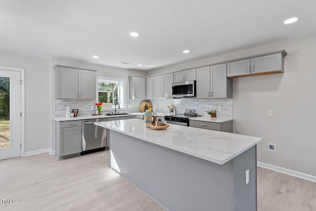 kitchen featuring appliances with stainless steel finishes, light wood-type flooring, light stone counters, sink, and a center island