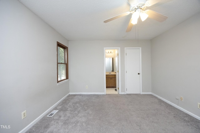 unfurnished bedroom featuring light carpet, a textured ceiling, ensuite bath, and ceiling fan