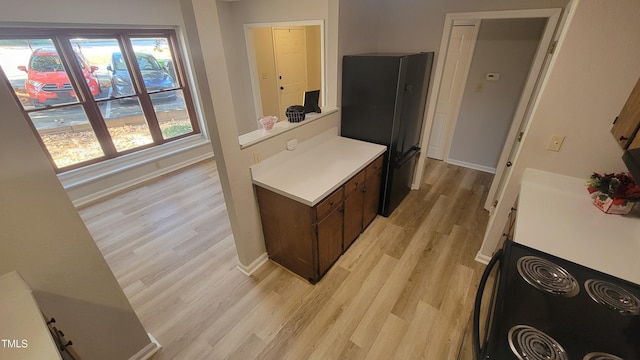 kitchen featuring dark brown cabinets, black refrigerator, range, and light hardwood / wood-style flooring