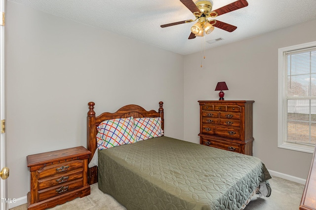 bedroom with ceiling fan, light colored carpet, and a textured ceiling