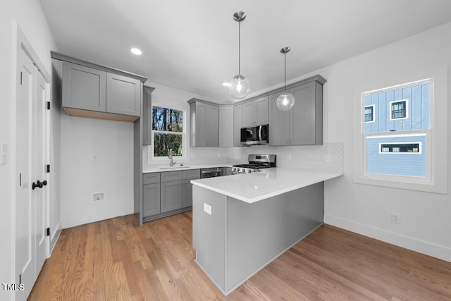 kitchen with kitchen peninsula, appliances with stainless steel finishes, decorative backsplash, light hardwood / wood-style flooring, and hanging light fixtures