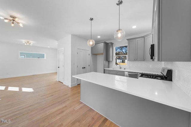 kitchen featuring kitchen peninsula, light hardwood / wood-style flooring, decorative light fixtures, and appliances with stainless steel finishes